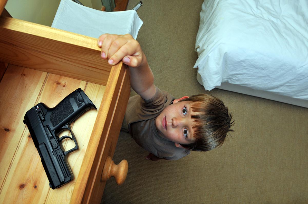 child looking up at drawer containing a gun